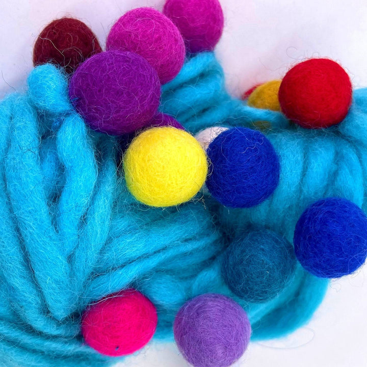 An up close view of the cyan blue felt ball wool yarn.  Showing the texture of the felt balls and the yarn. The felt balls are vibrant and rainbow in color.