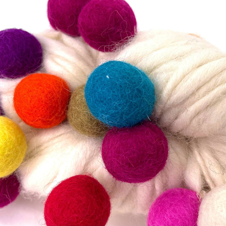An up close view of the white felt ball wool yarn.  Showing the texture of the felt balls and the yarn. The felt balls are vibrant and rainbow in color.
