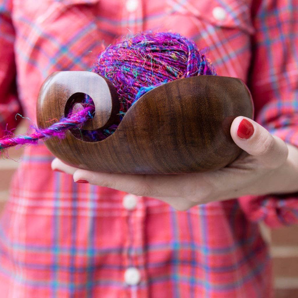 Woman's hand holding a brown wooden yarn bowl filled with purple yarn