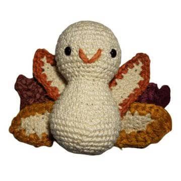 White amigurumi turkey with yellow, orange and brown feather tips on a white background