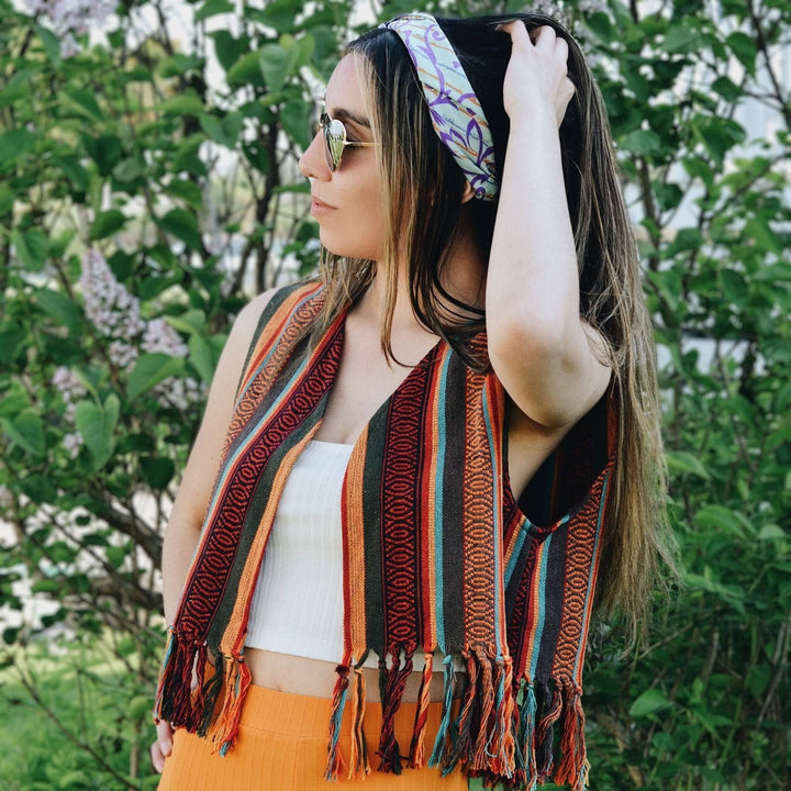 Model is wearing the red heather bolero vest in front of a bush.  