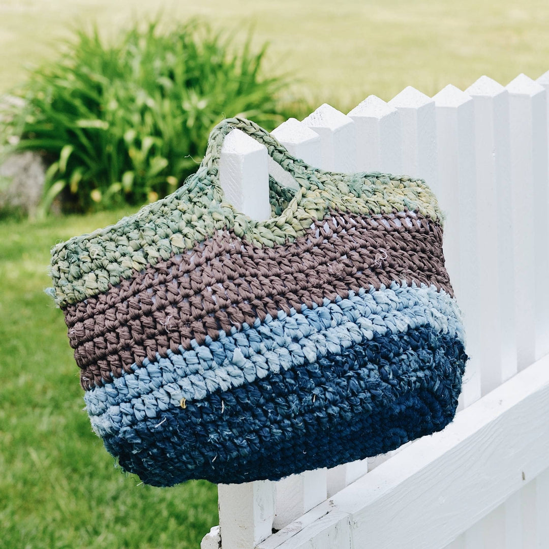 herbal dyed recycled silk yarn tote in deep sea hanging from a white fence.