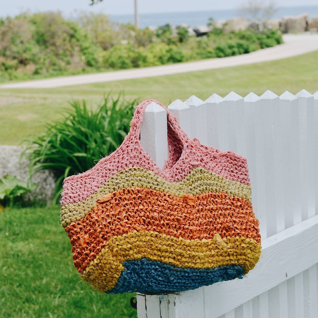 Knit herbal dyed recycled silk yarn tote in the flower pots colorway hanging from a white fence