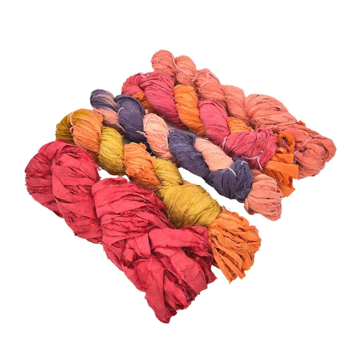5 skeins ribbon yarn multicolor warm pinks, reds, oranges in front of a white background. 