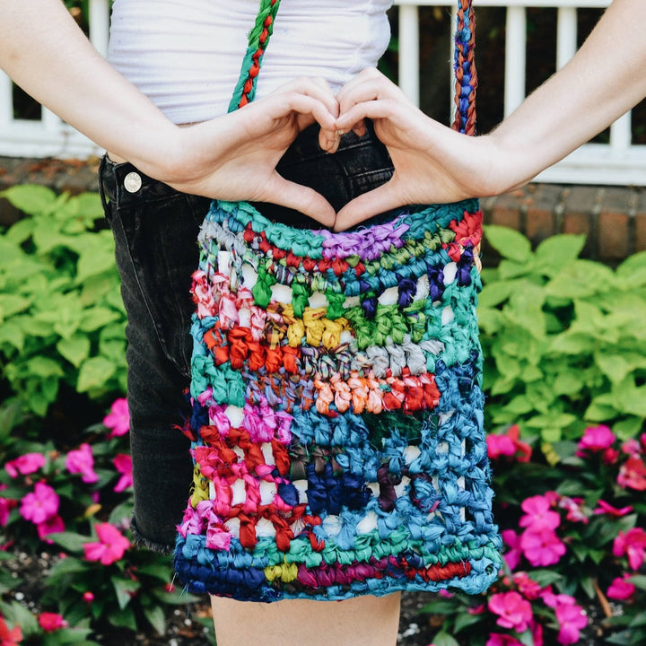 Closeup of model wearing the Hidden Heart Bag  around their shoulder. Model's hands are in a shape of a heart above the bag. 