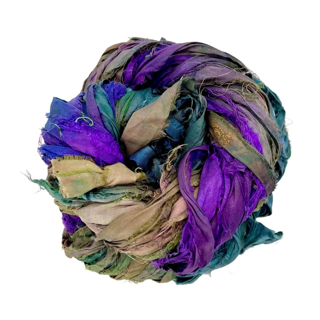 Single skein of sari silk ribbon yarn (purple, green, neutral) in front of a white background