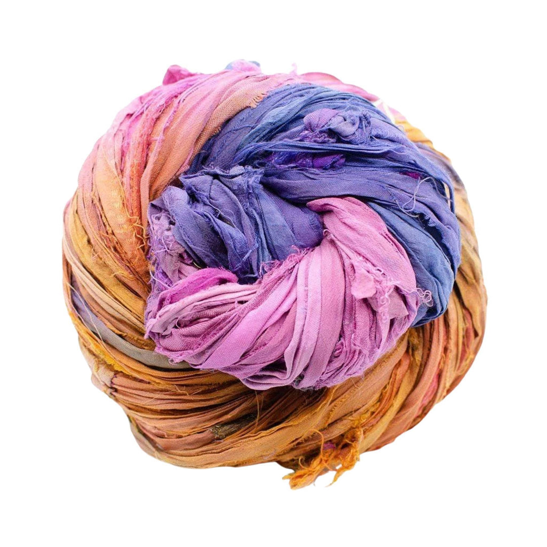 Single skein of sari silk ribbon yarn (pink, purple, and orange) in front of a white background