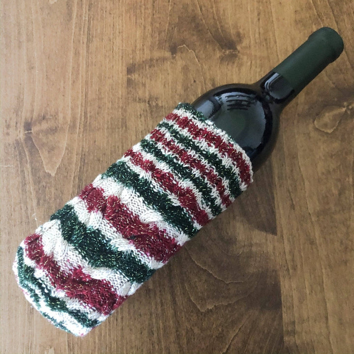 A red, green, and white wine bottle sleeve around a wine bottle laying on a wood background