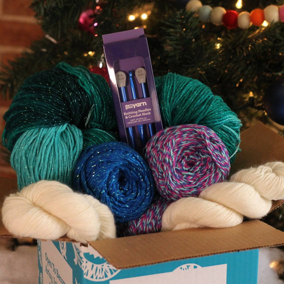 A closer look at some items included in the box. There's a triple twist light blue, dark blue and purple skein of sport weight yarn, classic sparkle blue worsted weight yarn, undyed white lace weight yarn and a new jumbo skein of sparkle green worsted weight yarn.