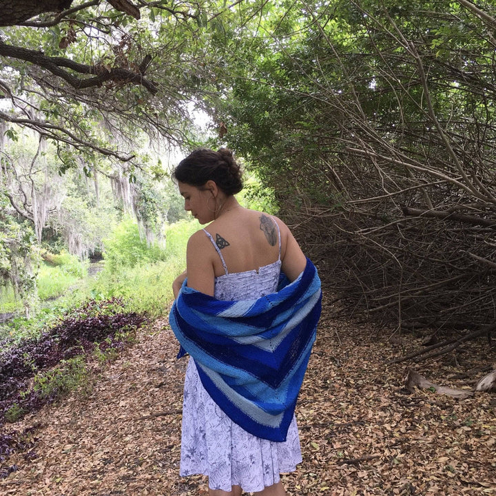 Designer standing in outside on a wooded path with multi hue blue shawl wrapped around them.