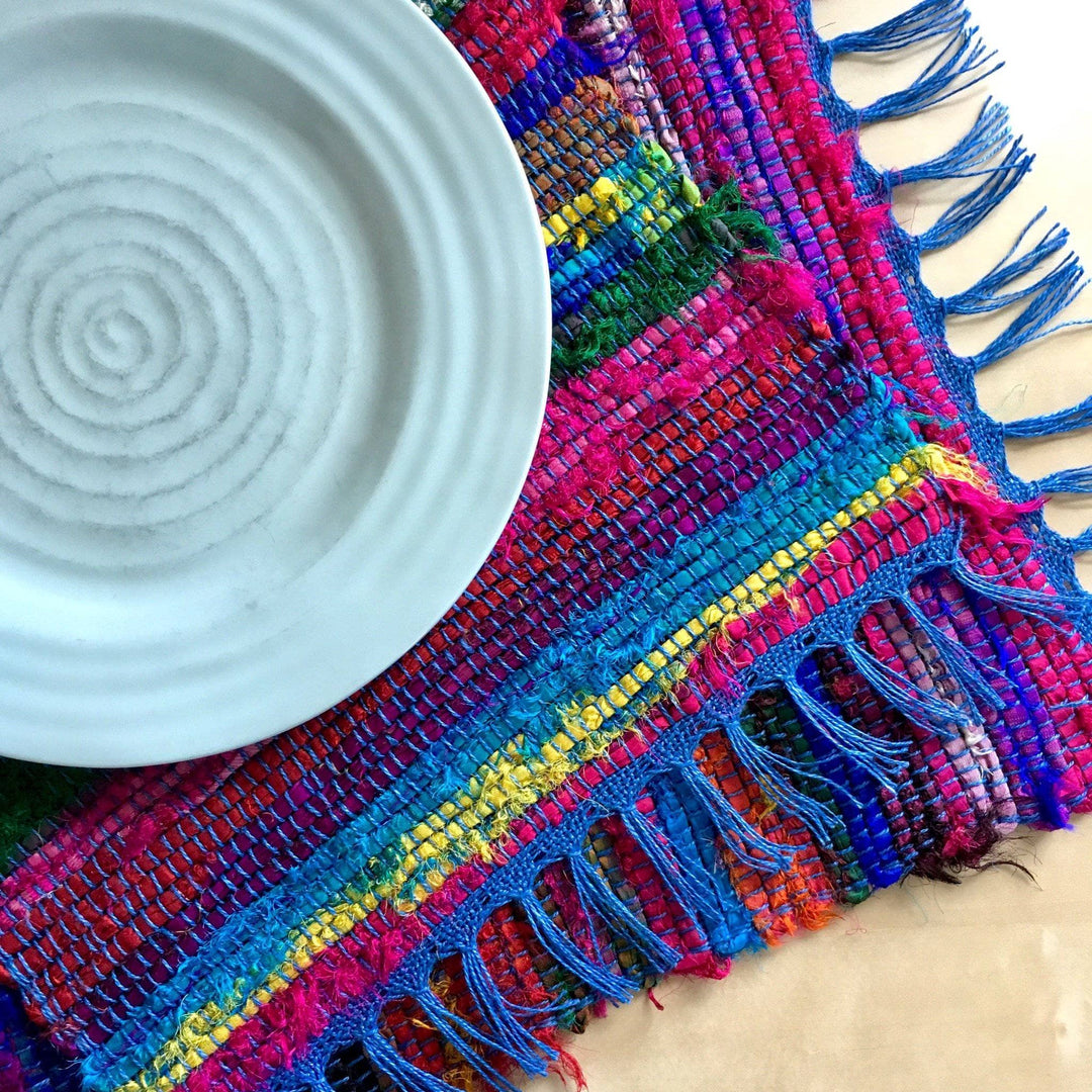 2 Tibet Jewels Woven Placemats stacked under a white bowl on a wooden surface