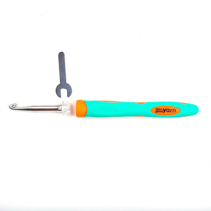 Teal and orange crochet hook handle, crochet hook attachment, and wrench tool in front of a white background.