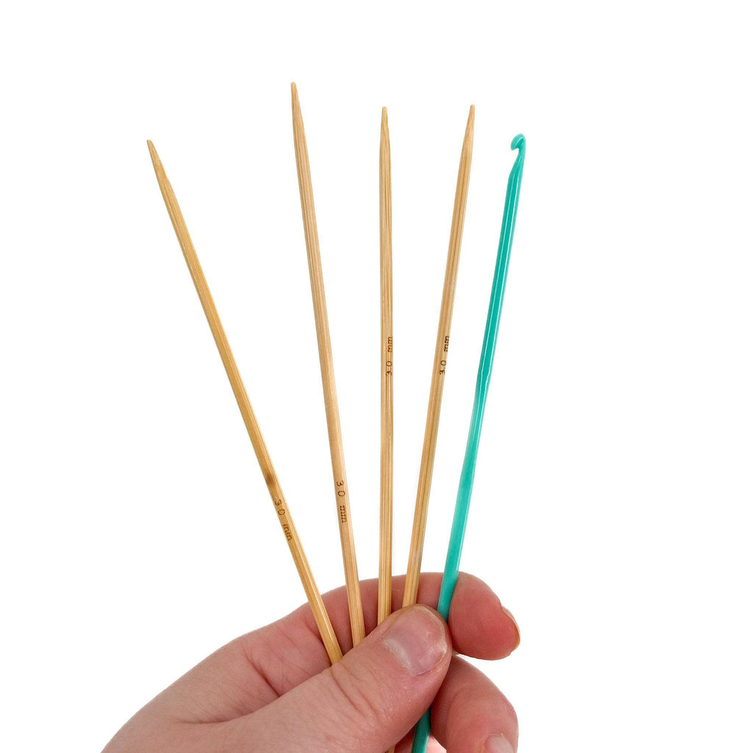 Close up image of four knitting needles and crochet hook that are included in the kit on a white background 