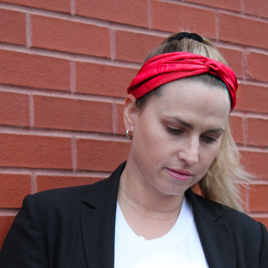Model is standing in front of a brick wall wearing a red kameela knot headband in her hair. 