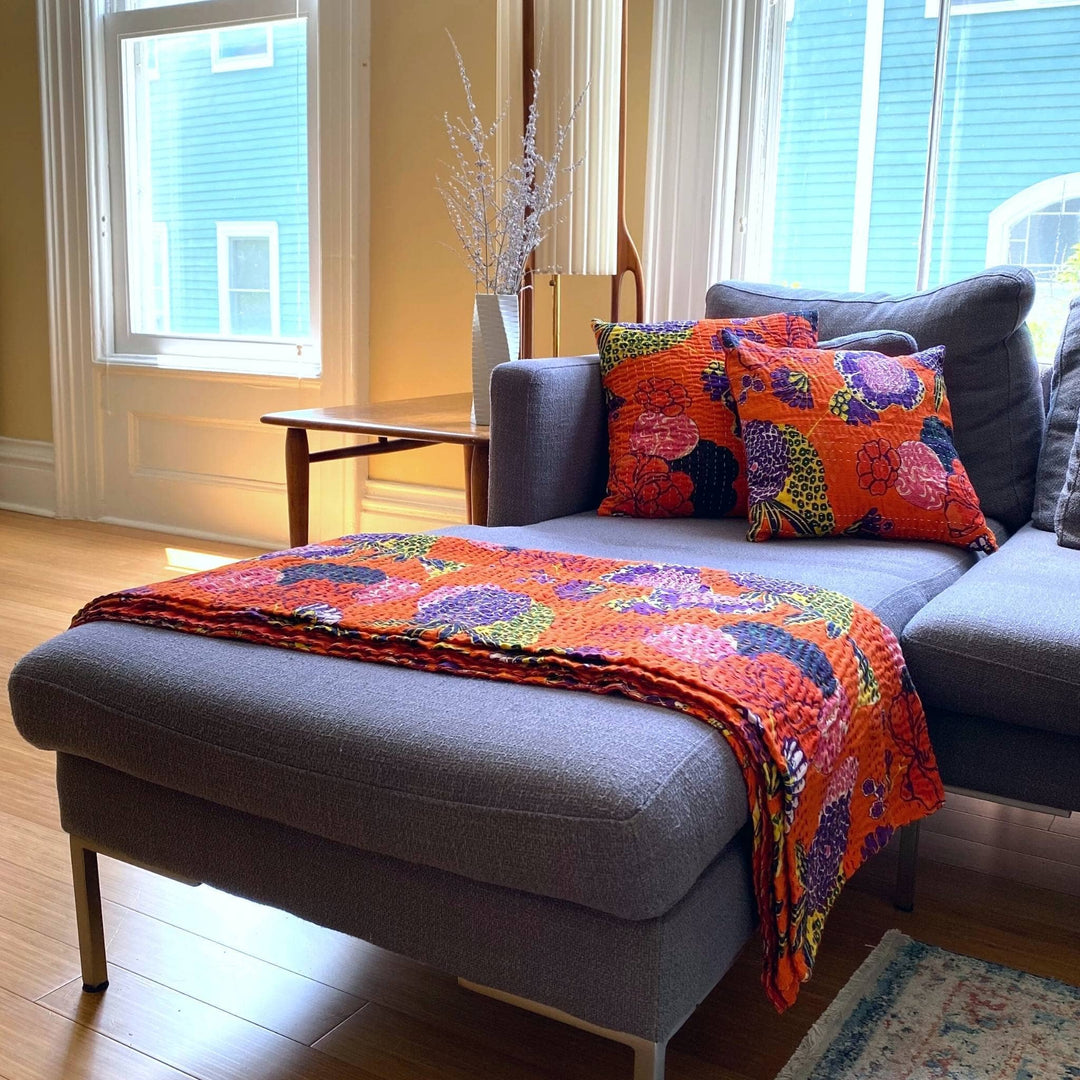 Orange symphony Kantha Quilt and Pillow Cover Set on a grey couch.  