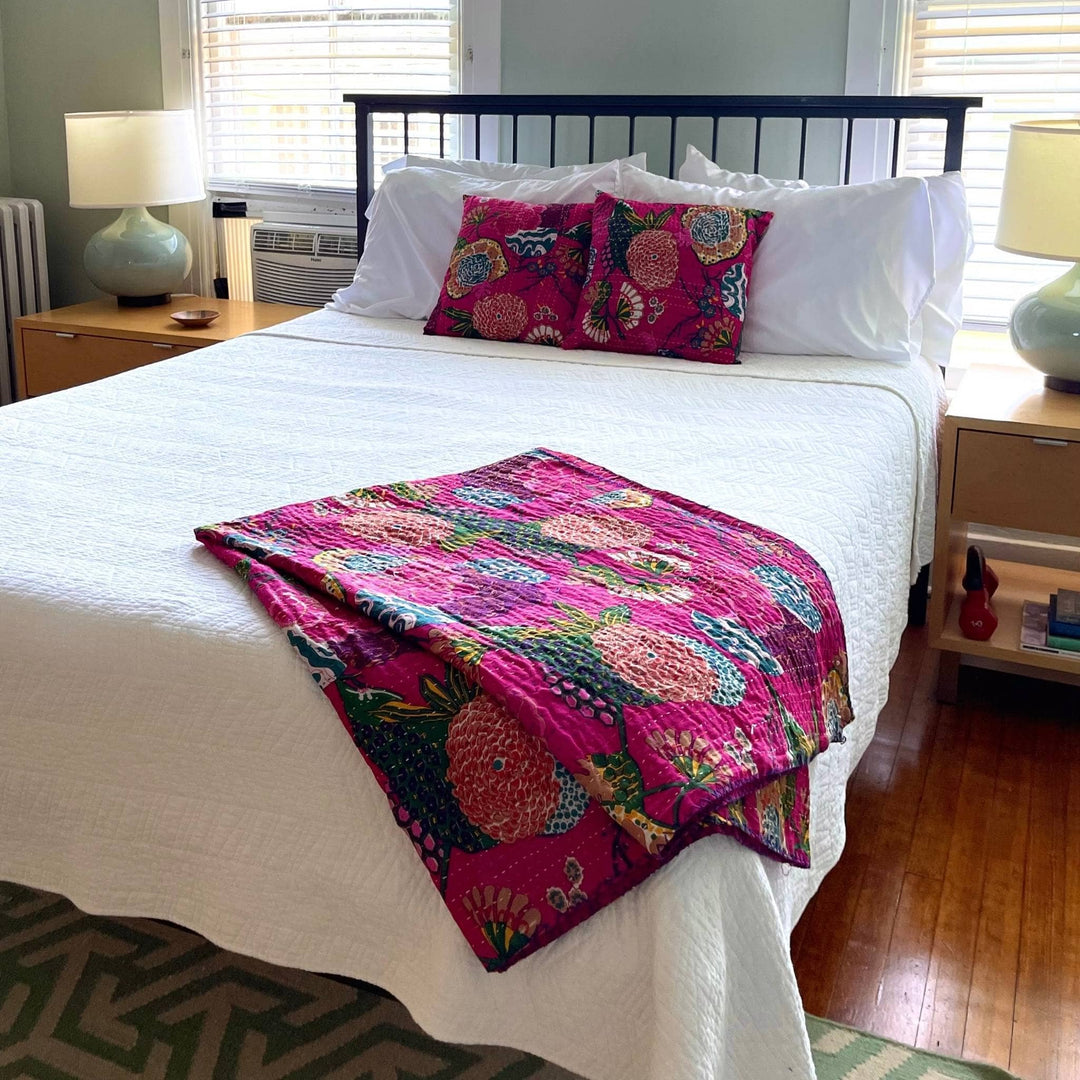 Pink kantha pillows and quilt on a bed with white bedding. 