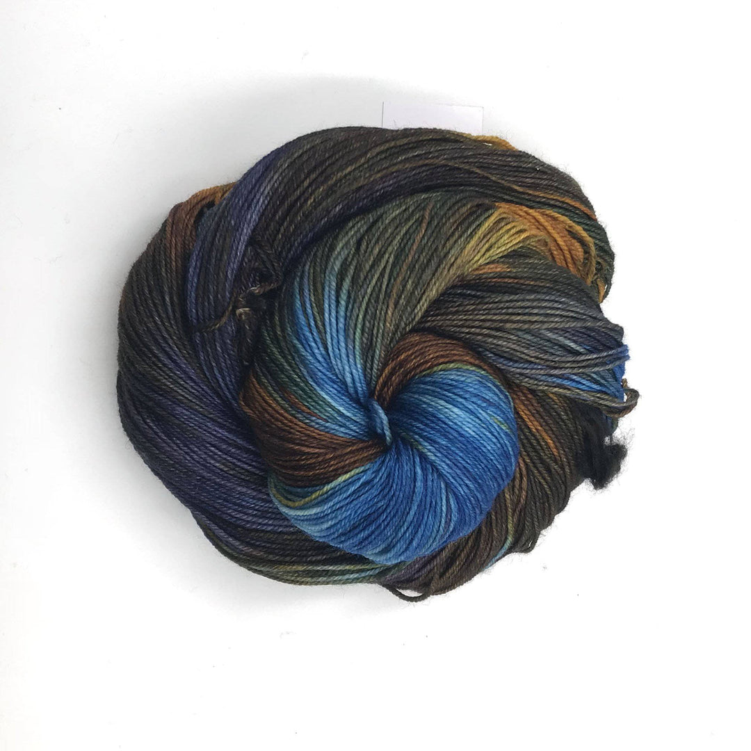 Superwash merino wool sock yarn ball in Ali (blue, brown) on a white background