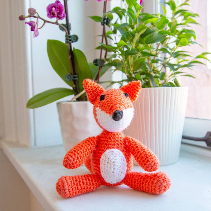 lifestyle shot of completed fox amigurumi kit sitting on a windowsill with potted plants in the background.