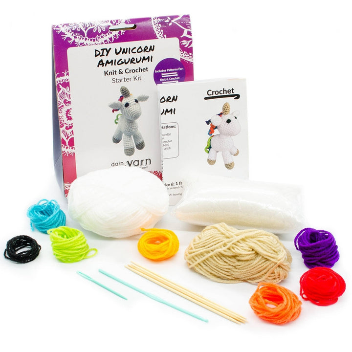 open unicorn amigurumi kit with all items showing in front of a white background. Yarn in multiple colors, knitting needles, crochet hook, tapestry needle, stuffing, and instructions.