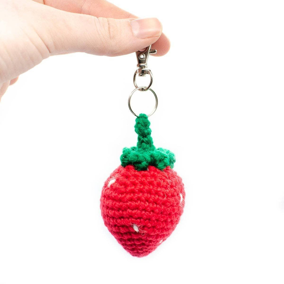 completed crochet strawberry keychain amigurumi kit being held up in front of a white background.