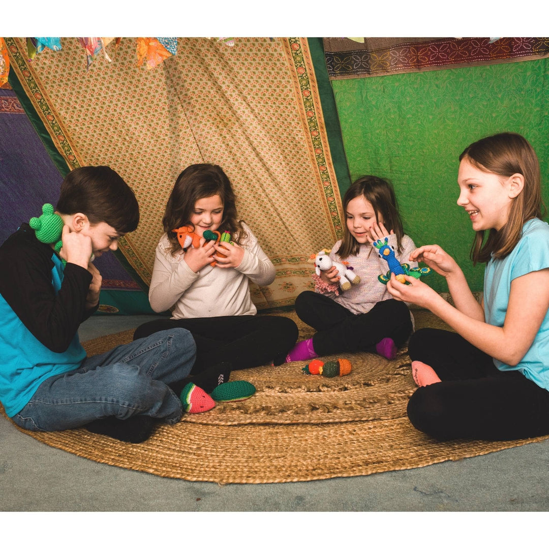 Group of kids playing with stuffed amigurumi toys on jute rug with sari silk canopy in the background.