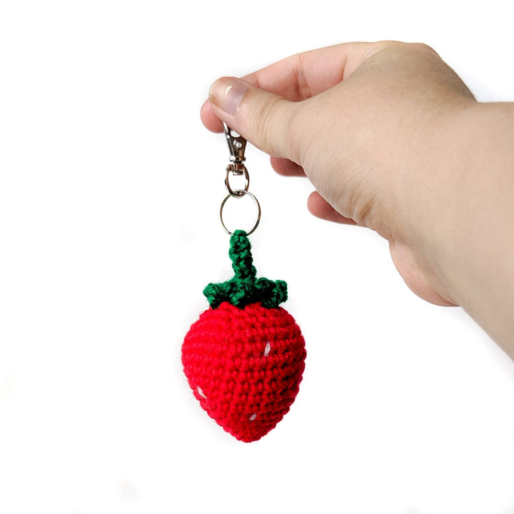 Red strawberry keychain being held on a white background