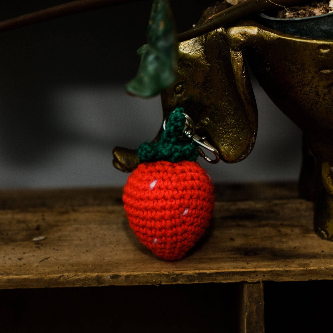 completed amigurumi strawberry keychain on wood shelf leaning against brass elephant planter.