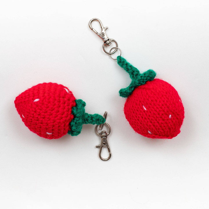 Crochet (left) and knit (right) strawberry amigurumi keychains in front of a white background. 