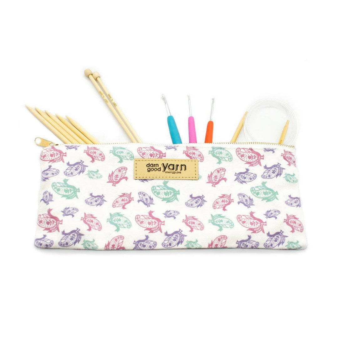 purple, green and pink paisley pouch with knitting needles and crochet hooks sticking out on a white backdrop.  