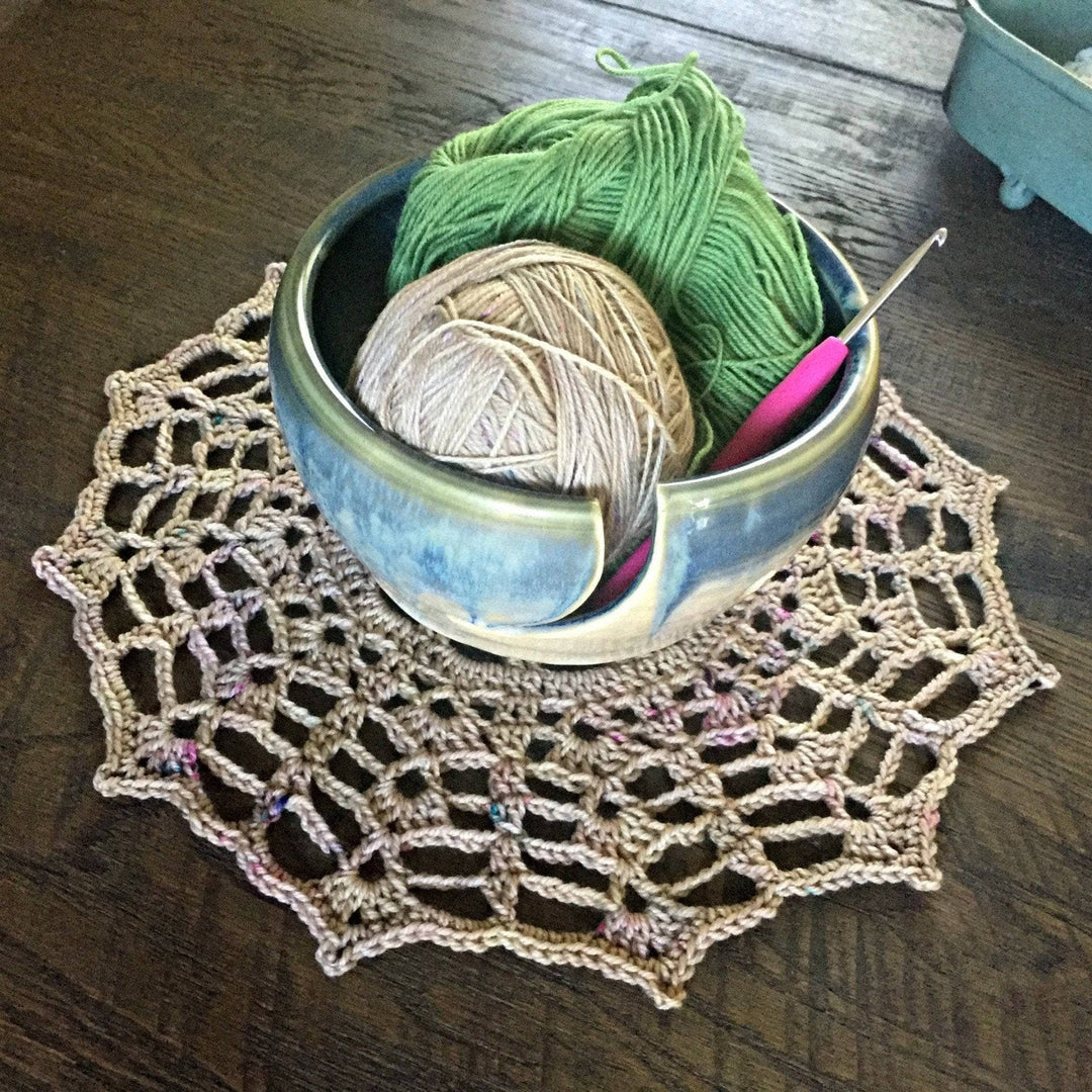 yarn bowl with yarn cakes inside and a hook over a table and a beige doily