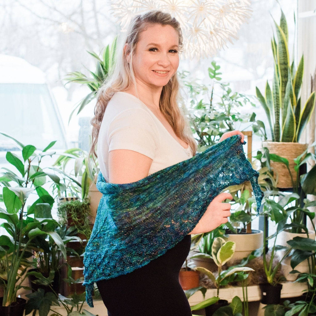 Model wearing lace weight silk shawl in enchanted forest with potted greenery in the background
