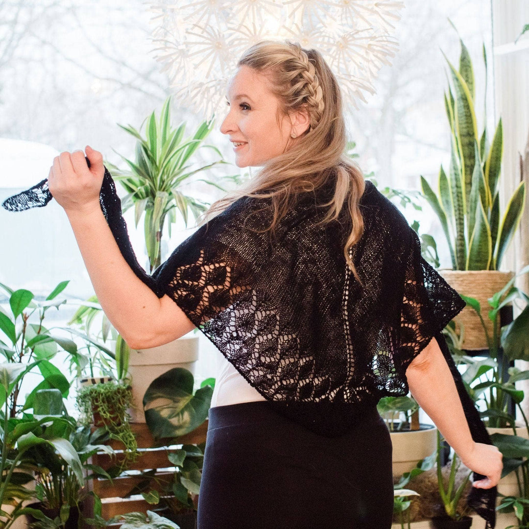 Model wearing lace weight silk shawl in black with potted greenery in the background