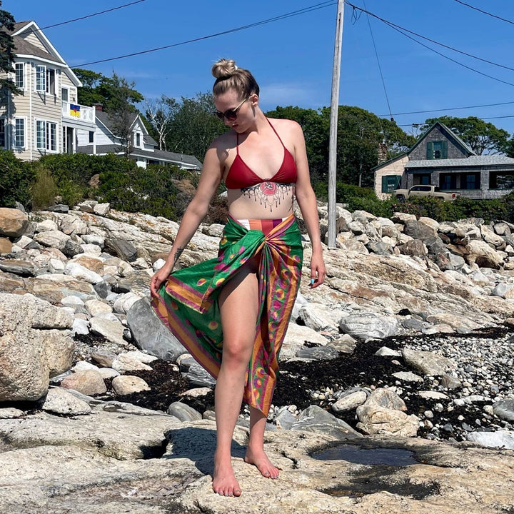 Model is wearing a green beach sarong while standing in front of some rocks on the beach.