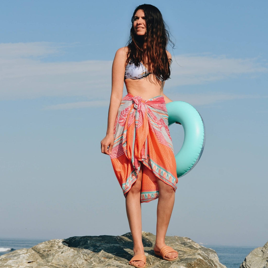 Model is standing on a rock wearing an orange sari silk beach sarong 