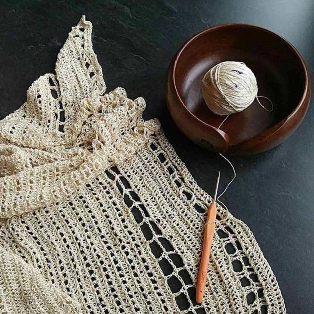 beige shawl over a black table and with a yarn bowl next to it