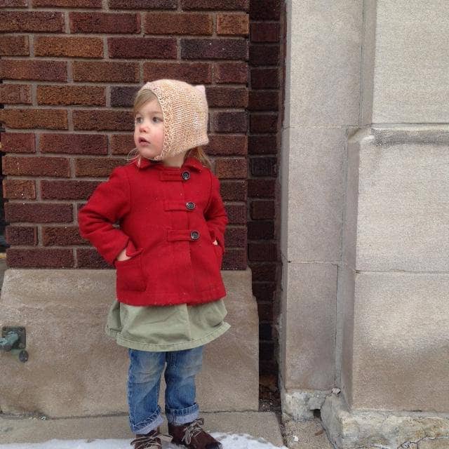 little girl looking to the side standing in front of a wall with a beige beanie