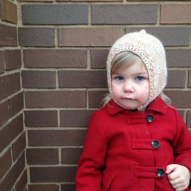 little girl standing in front of a wall with a beige beanie