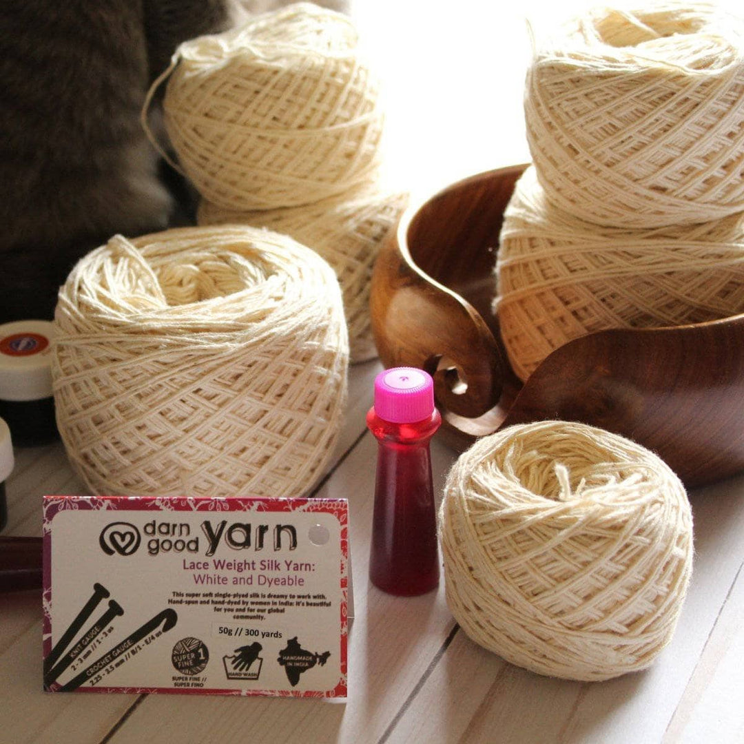 multiple cakes of white yarn with a tag of darn good yarn next to a wooden yarn bowl