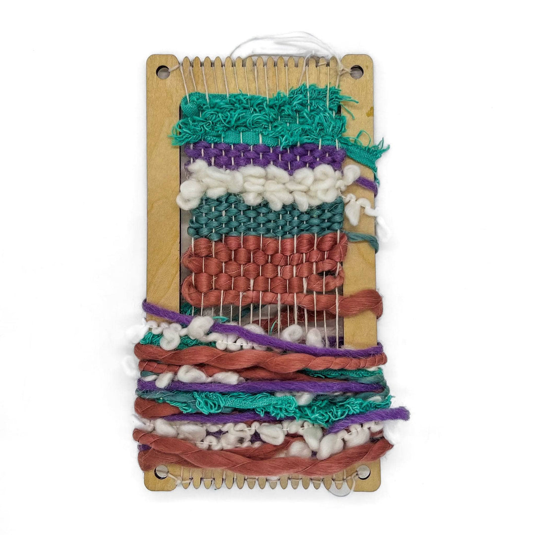 Mini loom with partially completed striped textured weaving project in progress in front of a white background.