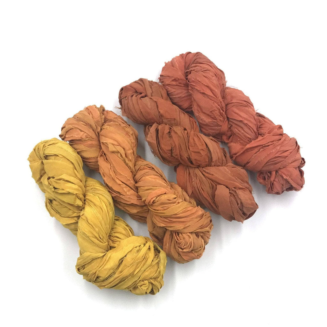 4 skeins of yellow and orange ombre ribbon yarn on a white background