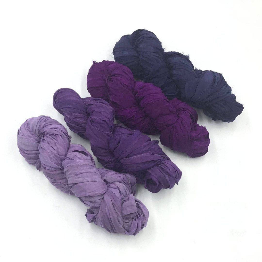 4 skeins of purple ombre ribbon yarn on a white background