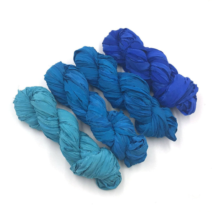 4 skeins of blue ombre ribbon yarn on a white background