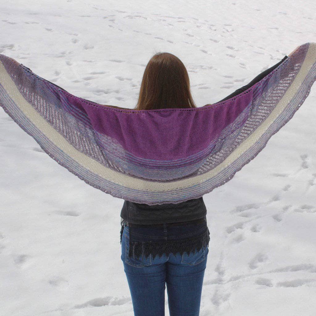 back of a woman holding a purple white and pink shawl with snow in the background