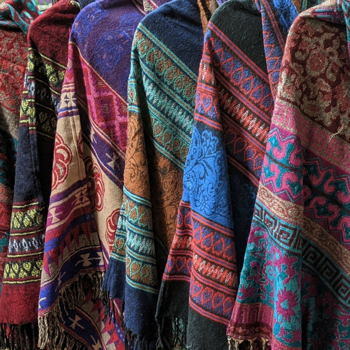 6 one of a kind nanda hooden ponchos hanging together to show variety in fabrics.