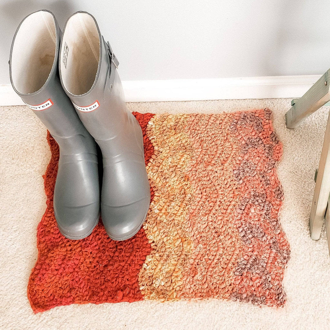 a red to pink ombre rug with grey boots on it