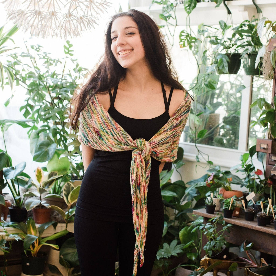 Model wearing unicorn cloud neon pop shawl tied at the front with potted greenery in the background. 