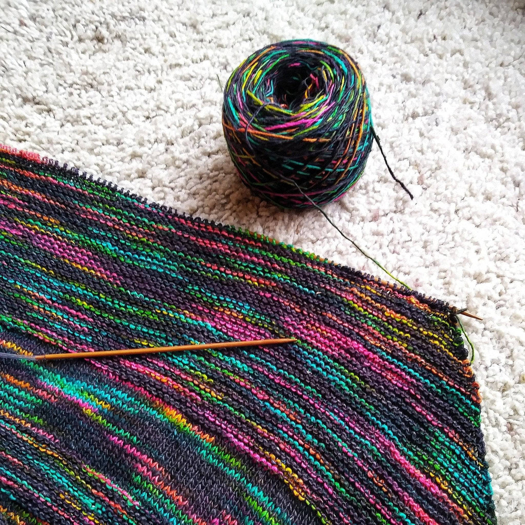 Black and rainbow shawl laying flat on a carpet
