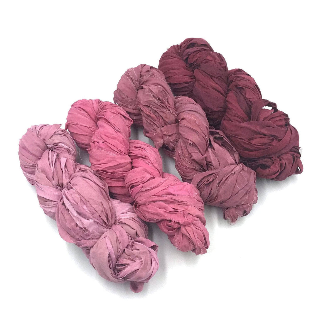 4 skeins of pink ombre ribbon yarn on a white background