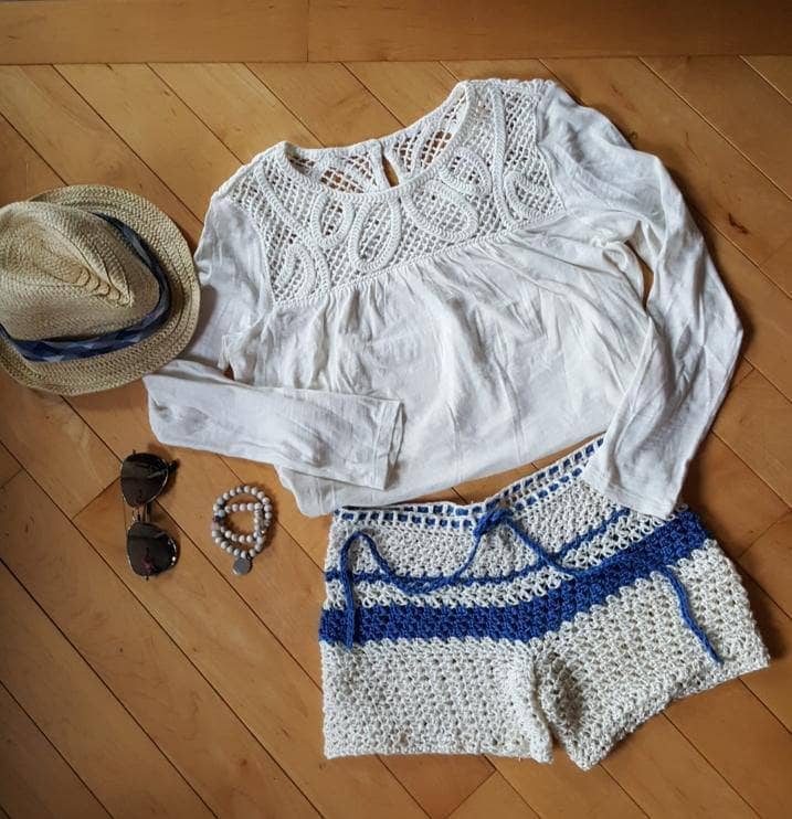 crochet shorts with a white top on the floor next to a hat and glasses