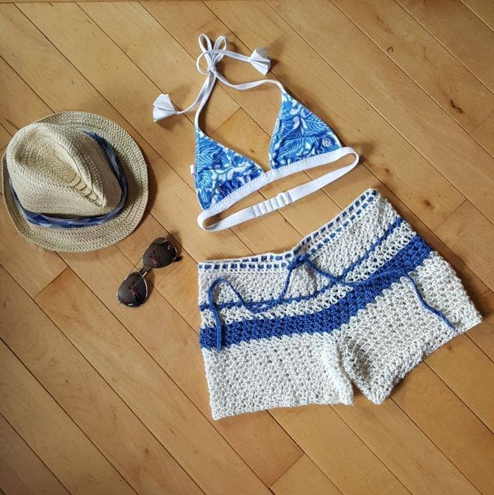 crochet shorts with a blue top on the floor next to a hat and glasses